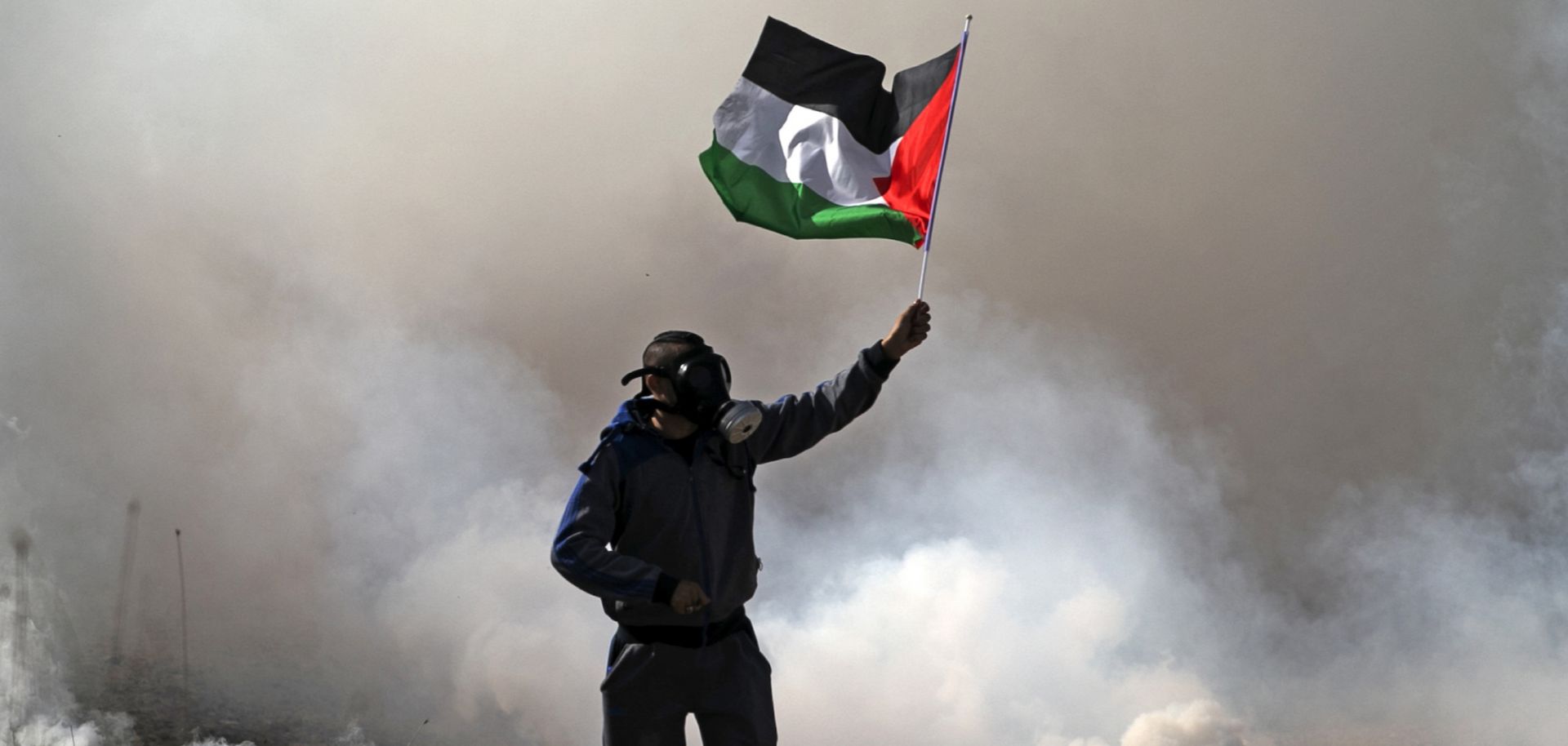 A protester waves the Palestinian flag amid smoke from tear gas fired by Israeli security forces during a demonstration near the West Bank village of Beit Dajan on Dec. 18, 2020. 