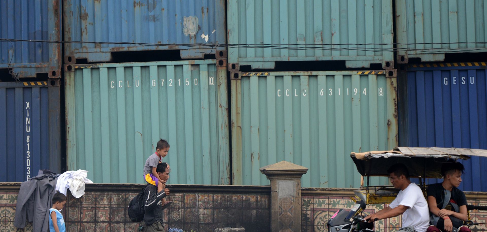 People pass a wall of shipping containers in Manila.