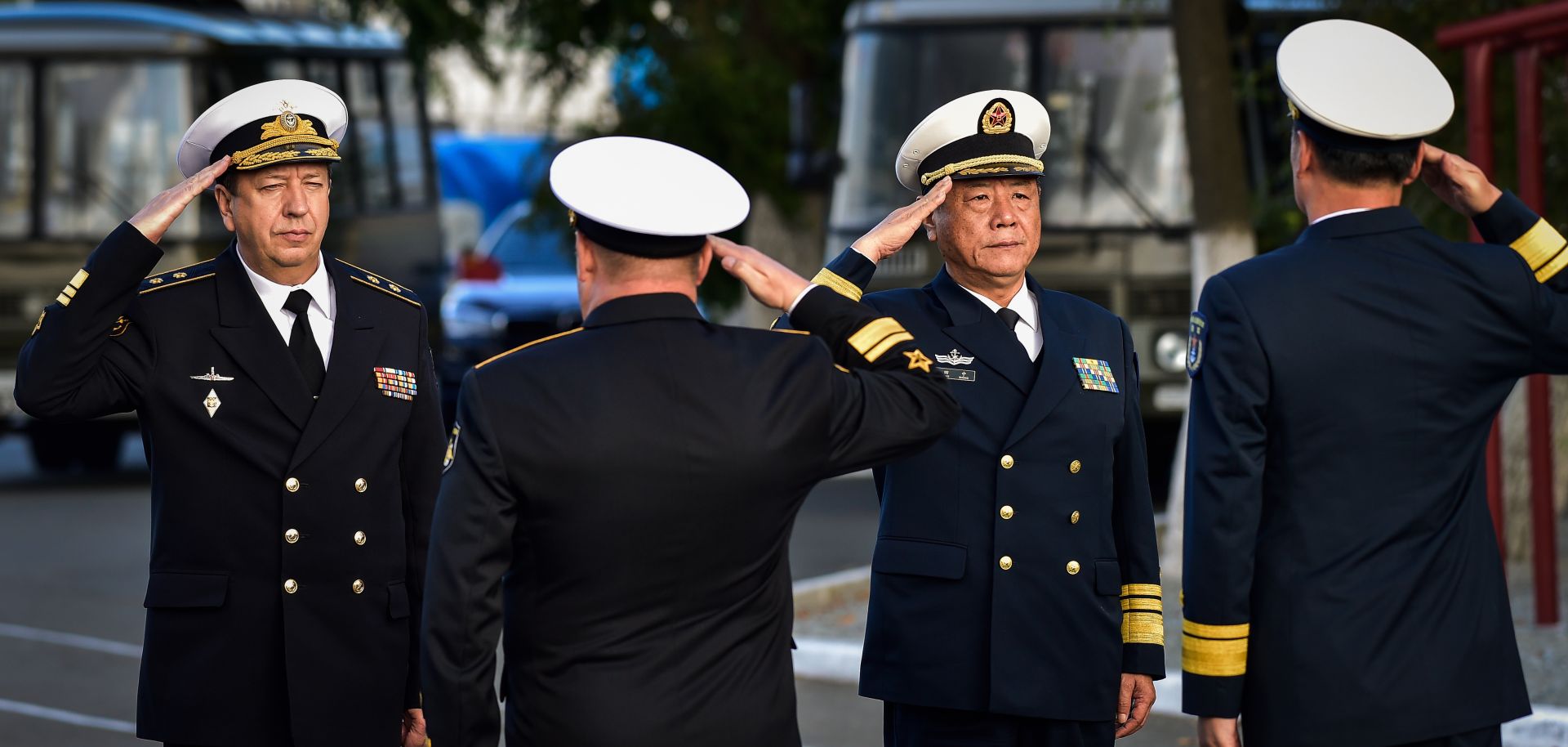 Military officials salute each other in a ceremony before Russia and China warships set out for a naval cooperation exercise.