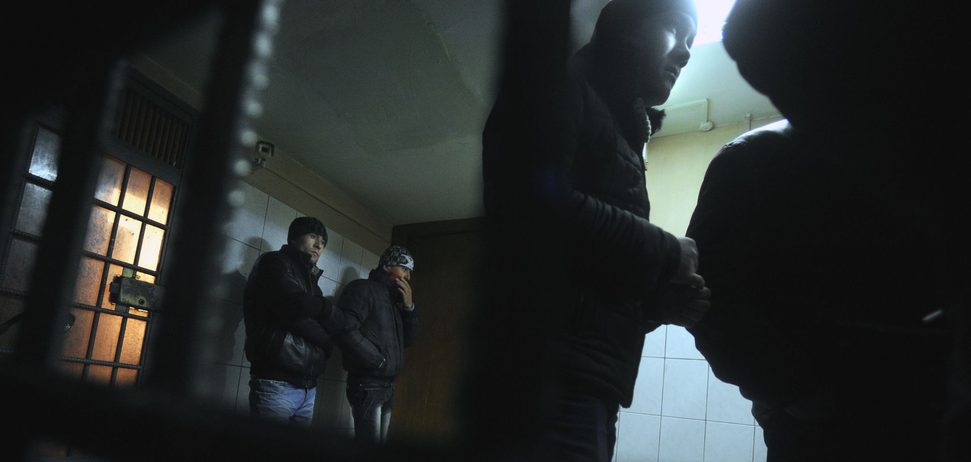 Illegal migrants from Uzbekistan stand behind the bars of their cell at a police station in the Kazansky railway station in Moscow.