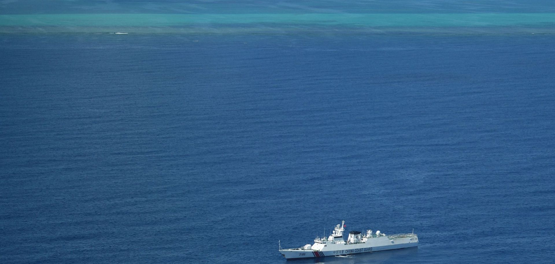 A photo taken during a Philippine surveillance flight on Sept. 28, 2023, shows a Chinese coast guard ship on patrol near the Scarborough Shoal (seen in the background) in the South China Sea.