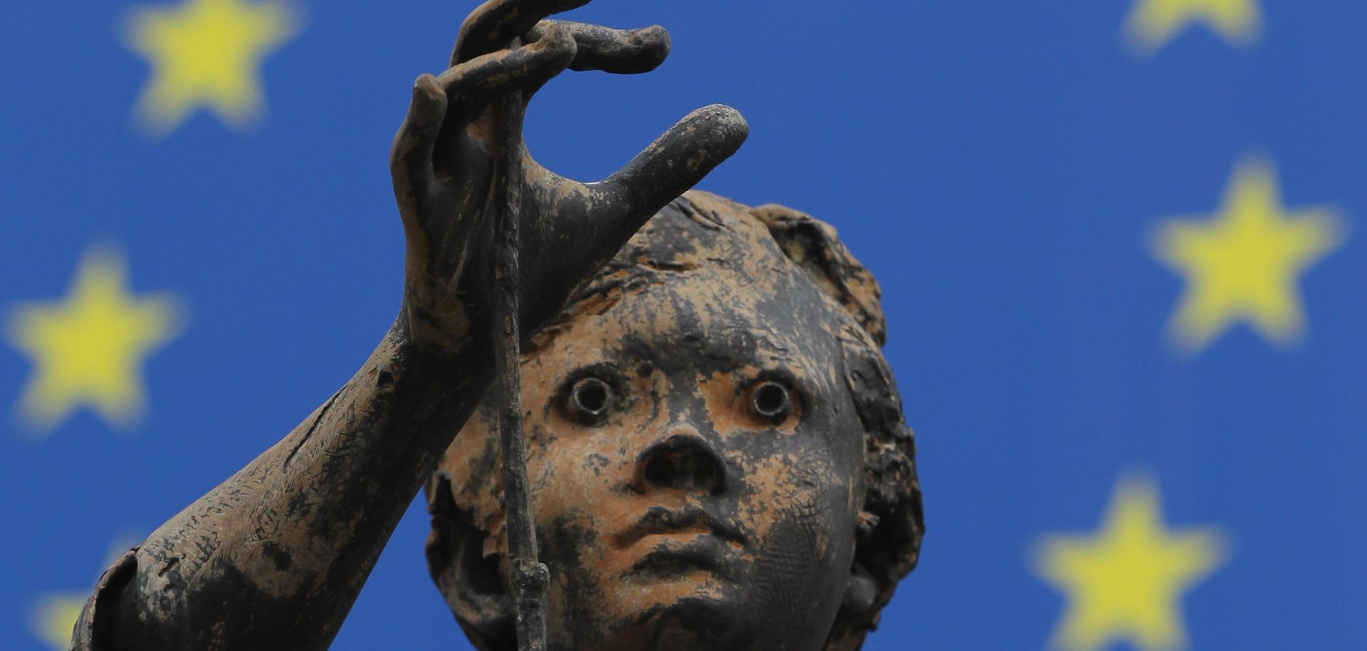 One of the sculptures of young girls by artist Rene Julien stands in front of a flag of the European Union