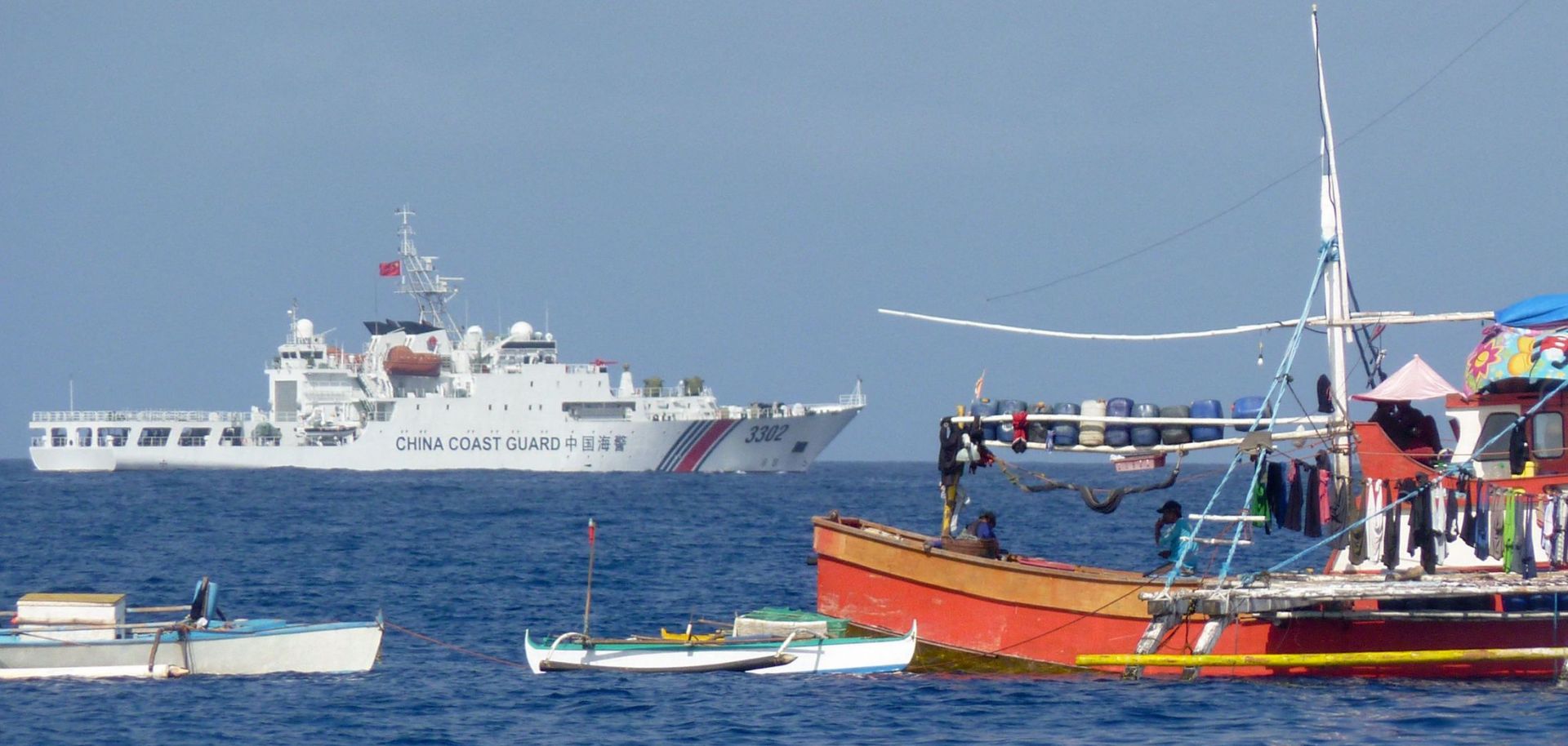 A Chinese coast guard ship sails past anchored Philippine fishing boats in the Scarborough Shoal, in the disputed South China Sea, on Feb. 3, 2023.