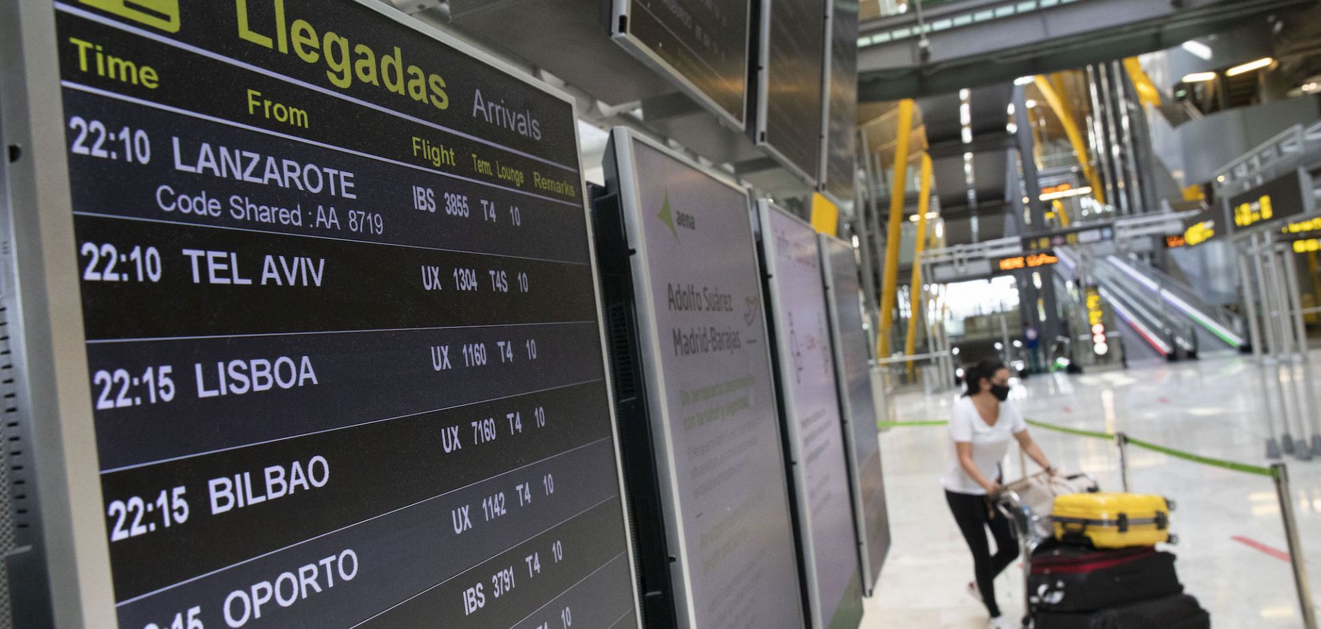 A travelers carry her luggage as she walks past an arrivals flight information display at Adolfo Suárez Madrid-Barajas airport on June 07, 2021 in Madrid, Spain. Spain, the world's second most visited tourism destination, has re-opened borders to vaccinated visitors worldwide as well as non-vaccinated Europeans with a negative antigen test.