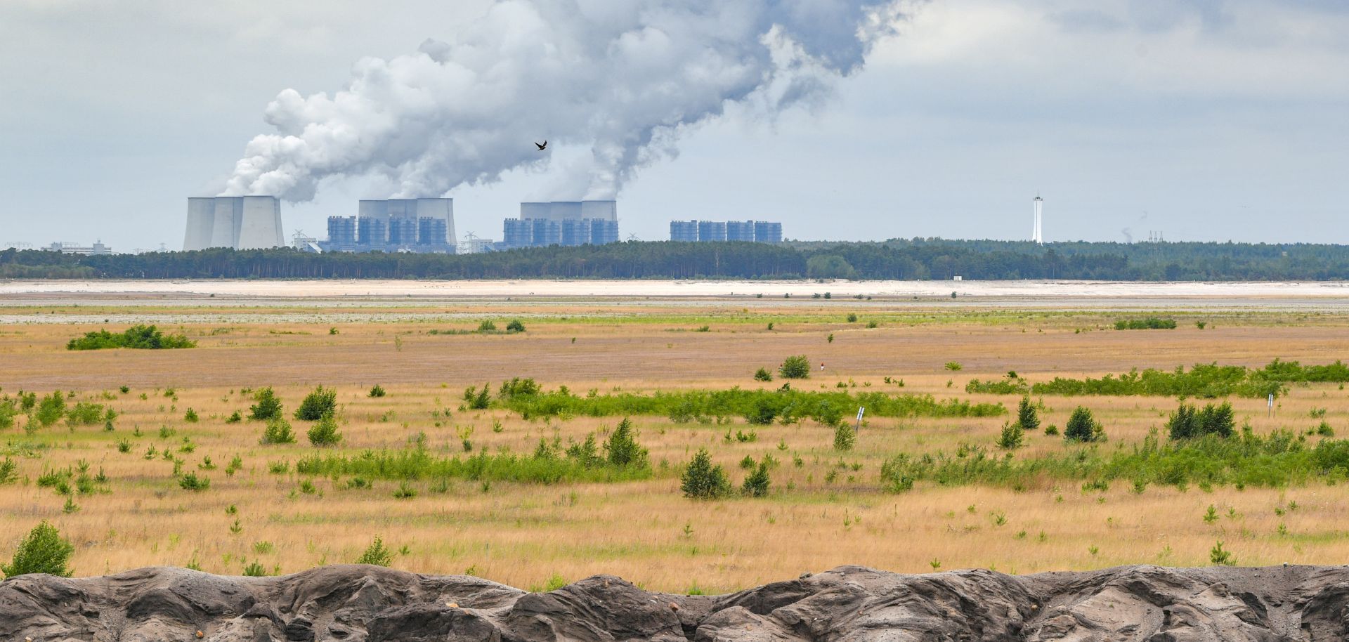 Steaming cooling towers of the Jänschwalde lignite-fired power plant can be seen behind a large field.