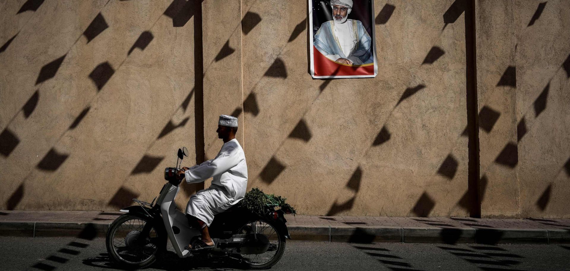 A man rides a motorcycle past a wall of the Nizwa fort bearing a portrait of Omani Sultan Qaboos bin Said in February.