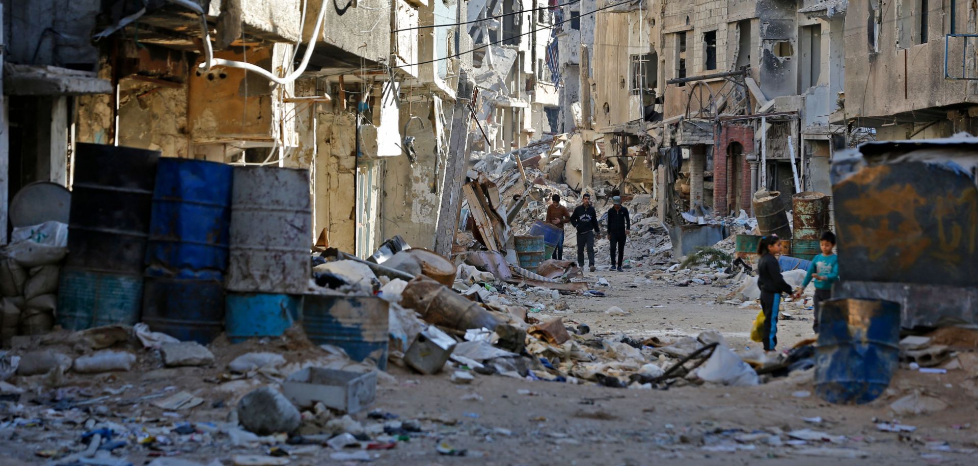 People walk amid rubble of destroyed buildings in a street in the Tadamun neighborhood near the Palestinian Yarmuk camp in southern Damascus on Nov. 3, 2018. 
