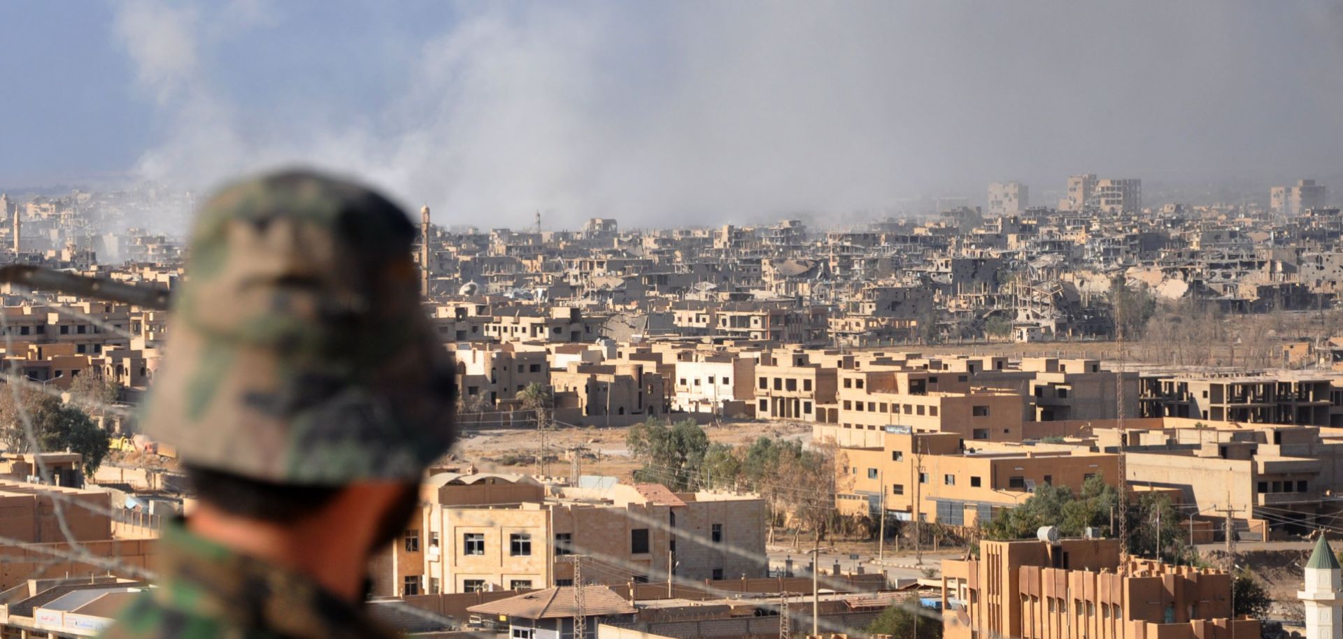 A member of the pro-Syrian government forces watches as smoke rises from buildings in the eastern Syrian city of Deir el-Zour after a Russian airstrike targeted Islamic State militants.