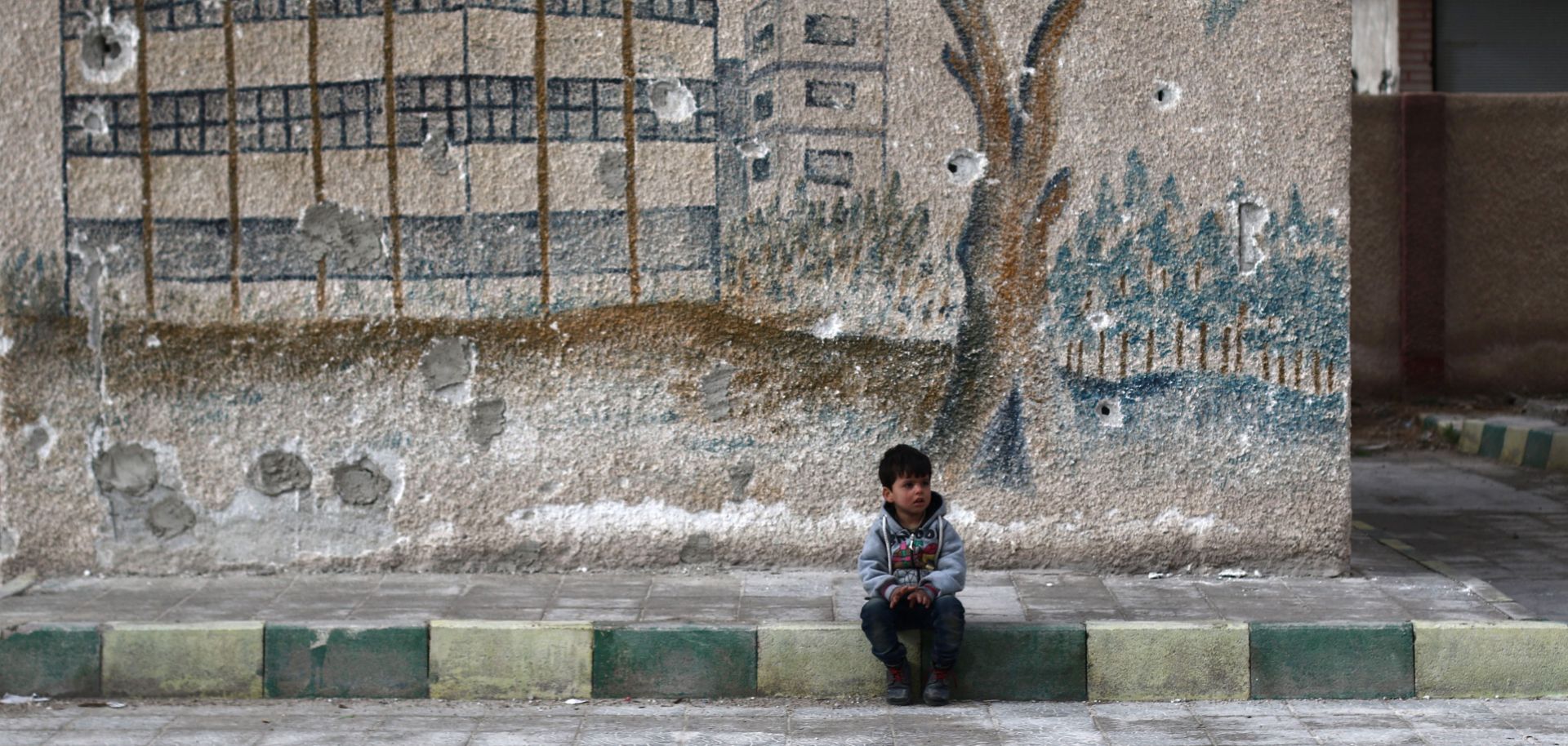 A child sits in front of the bullet-riddled wall of a former school in Syria's eastern Ghouta, a rebel-held area on the outskirts of Damascus, on Jan. 5, 2016.