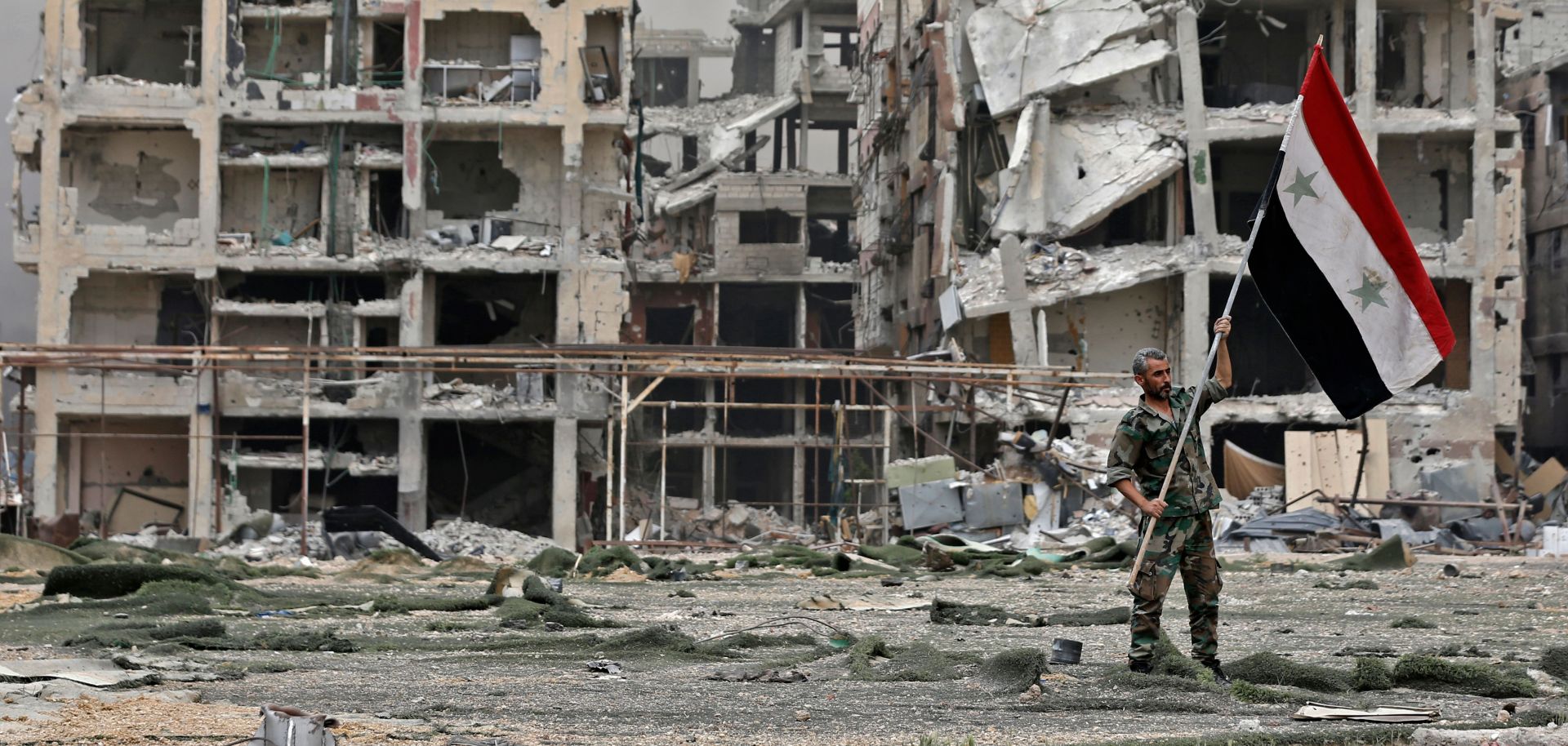 A member of the Syrian pro-government forces plants the national flag in front of damaged buildings in the Yarmouk Palestinian refugee camp on the southern outskirts of the capital Damascus during May 2018.