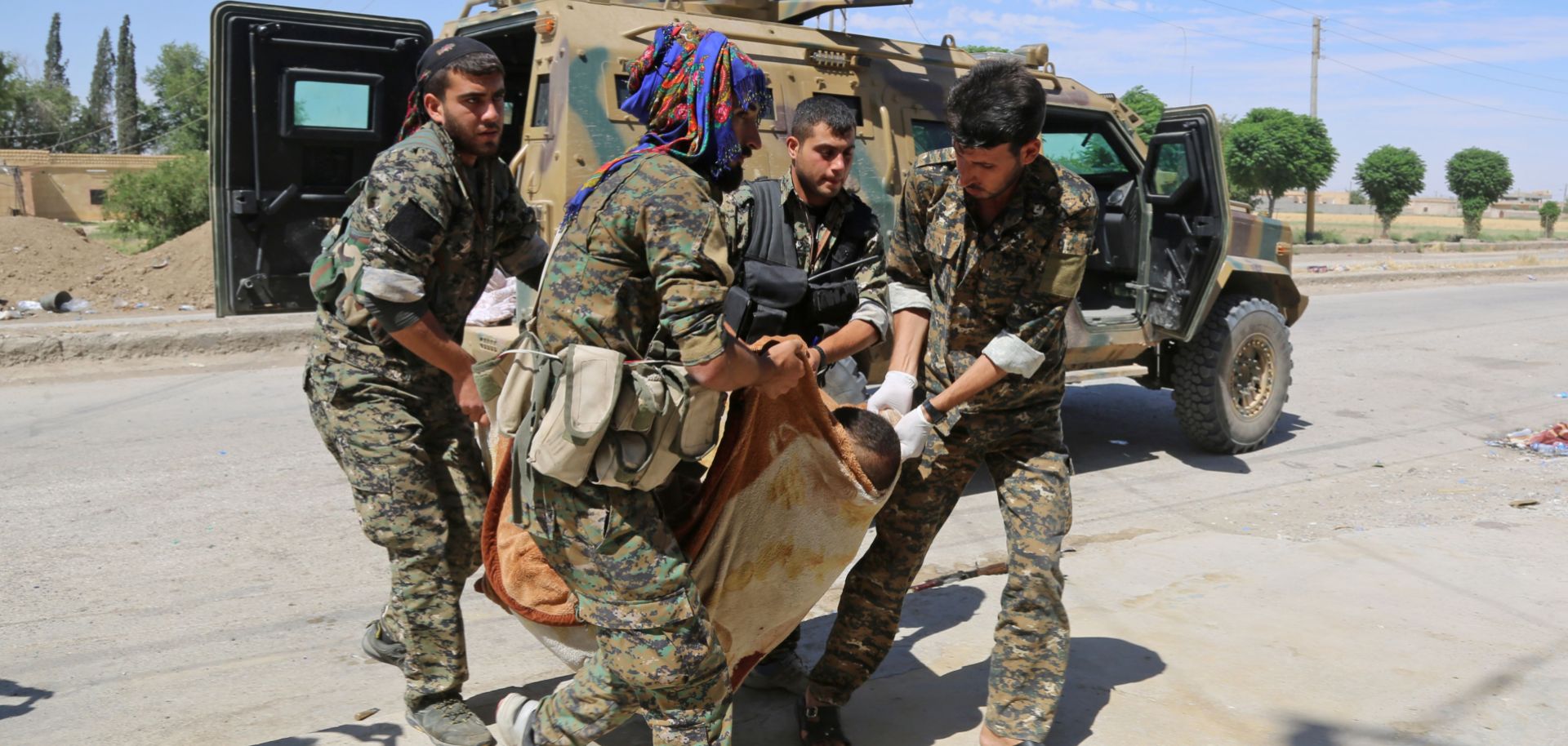 Members of the U.S.-backed Kurdish People's Protection Units carry a wounded Kurdish fighter to a field hospital near the northern Syrian village of Raqqa Samra on June 21, 2017.
