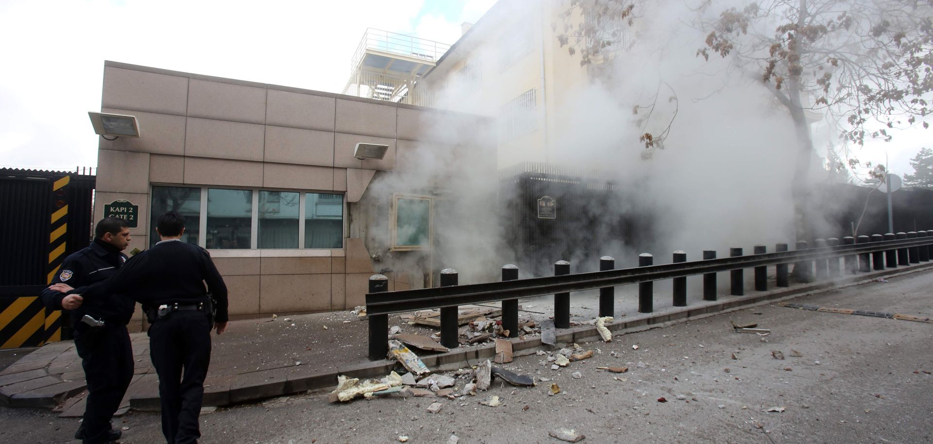 People stand outside the US Embassy as smoke fills the air.