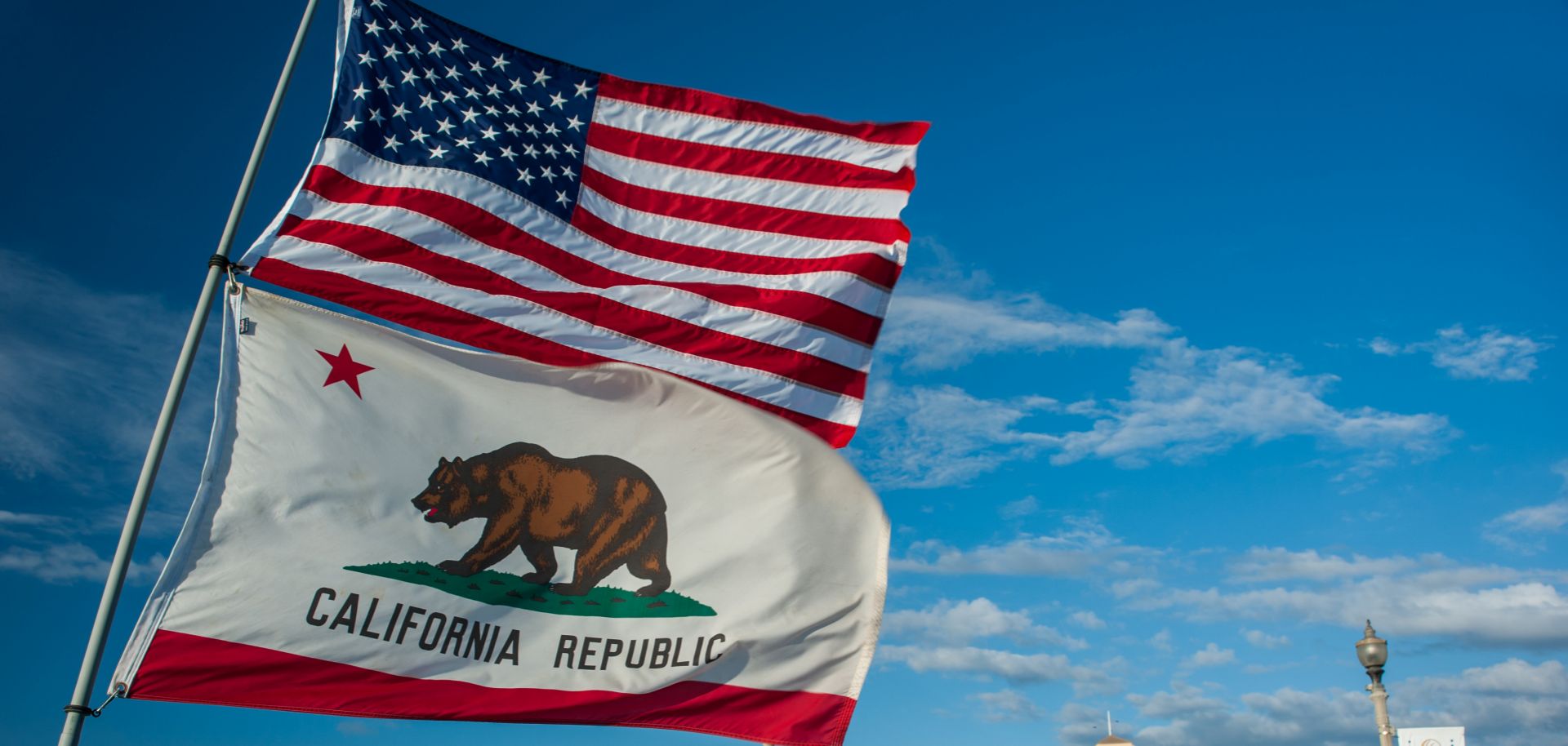 The flags of the United States and America and the state of California flap against an azure sky. 
