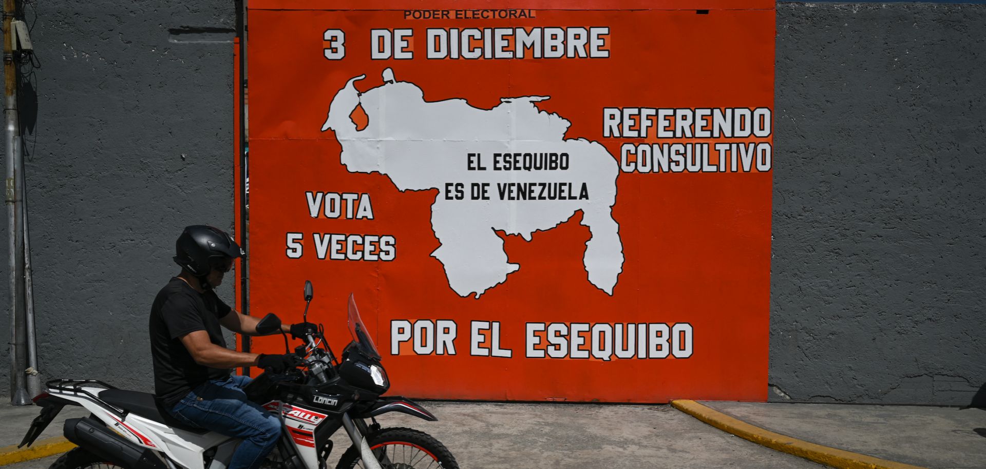 A man on a motorcycle rides past a mural in Caracas, Venezuela, campaigning for a referendum on annexing the Guyana-administered region of Essequibo on Nov. 28, 2023. 