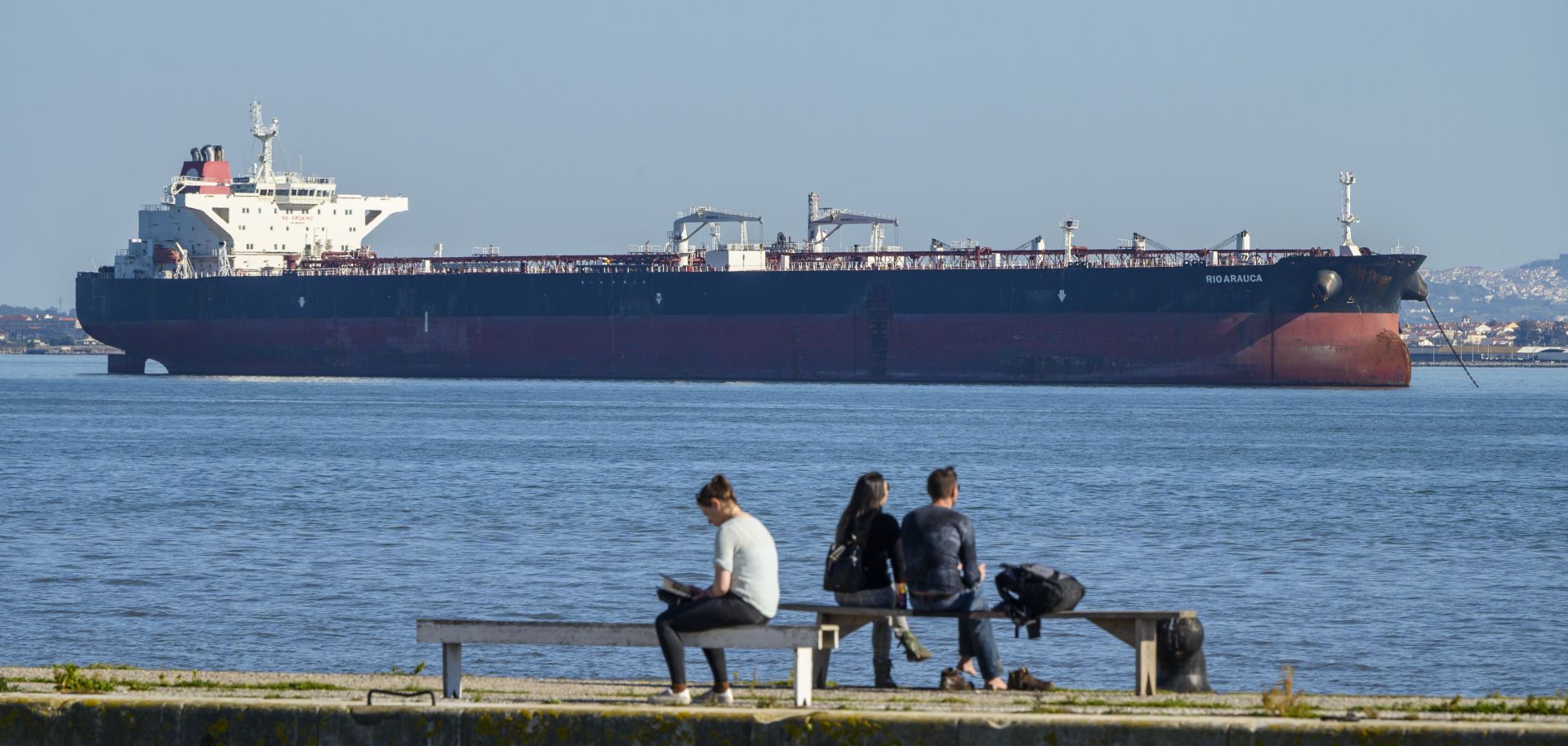 People relax on the bank of the Tagus River where Venezuelan PDVSA oil tanker Rio Arauca lies at anchor, having been impounded by Portuguese authorities for nearly two years due to unpaid debt, March 9.  