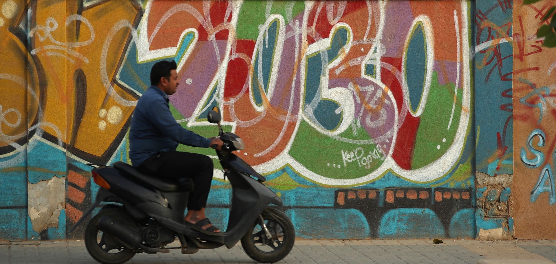 A man rides past graffiti alluding to Vision 2030