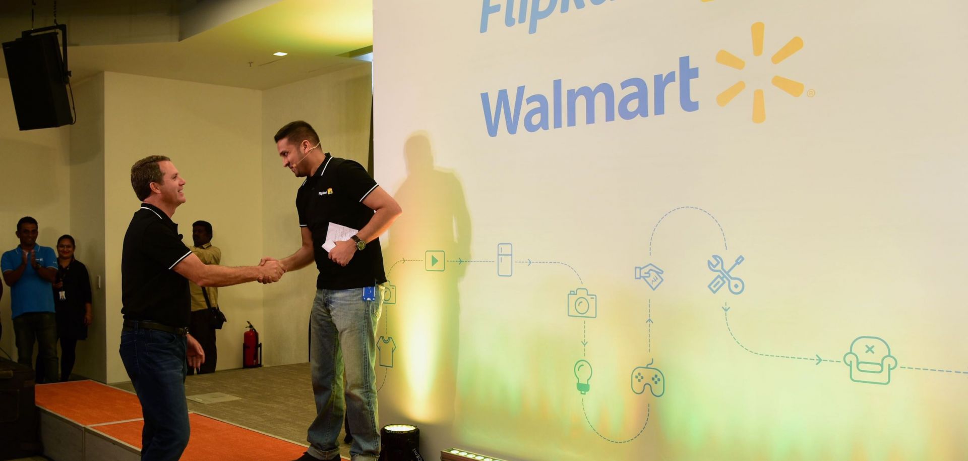 The CEOS of Walmart and Flipkart shake hands at an event in India.