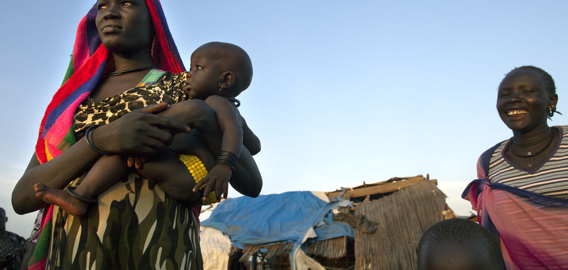  A woman from the Dinka tribe stands with her baby at a small settlement outside the city center