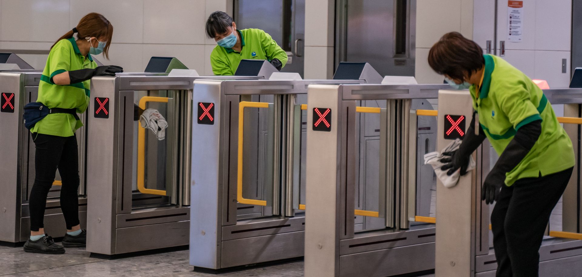 Cleaners wearing protective masks clean the gate in the arrival hall at a Hong Kong rail station on Jan. 29, 2020.