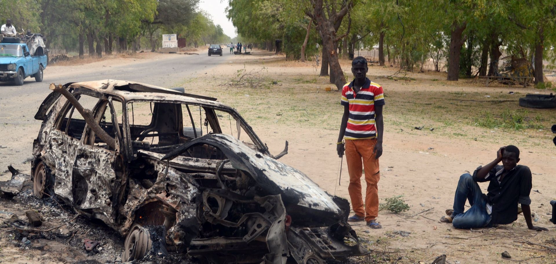 People stand by the wreckage of a car that has been blown up.