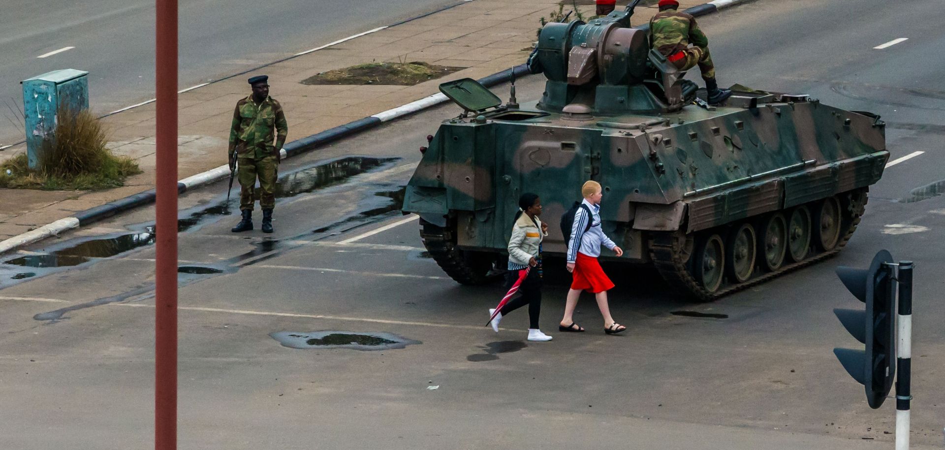 Two young women walk past an armored personnel carrier in Zimbabwe's capital, Harare, under the watch of soldiers regulating traffic.