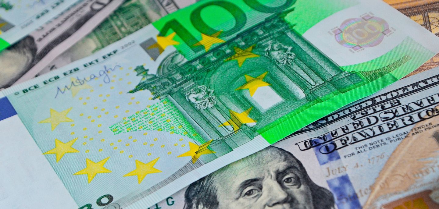 Euro banknotes lie atop U.S. dollar banknotes.