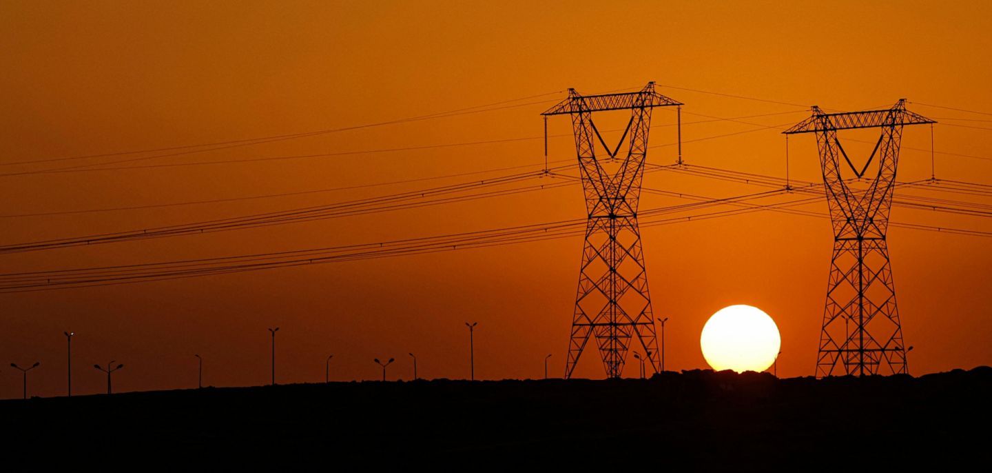 The sun sets behind high voltage transmission towers along a highway in El-Shorouk, about 47 kilometers outside the city center of Cairo, on July 24, 2023. 