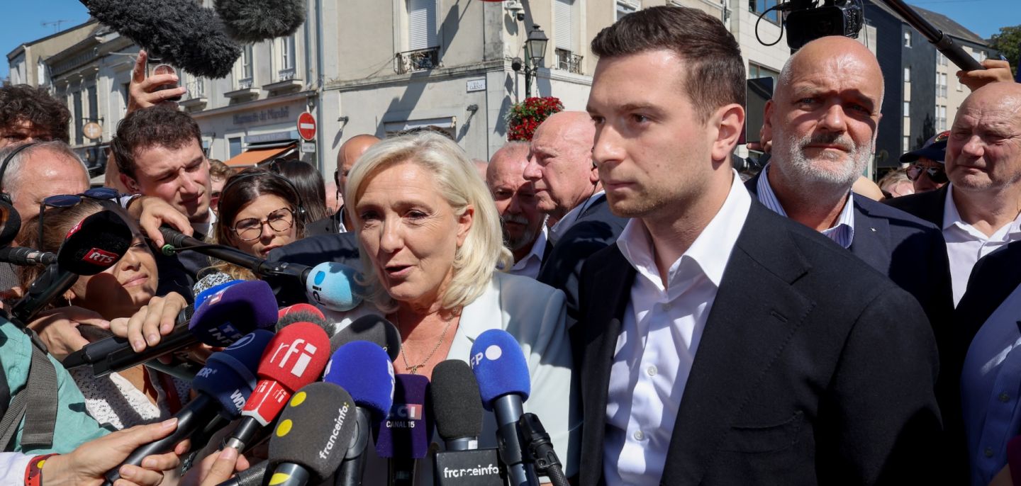 Journalists surround French far-right National Rally leader Marine Le Pen (center) as she arrives with National Rally president Jordan Bardella (third from right) for a campaign rally in La Fleche, France, on July 8, 2026.