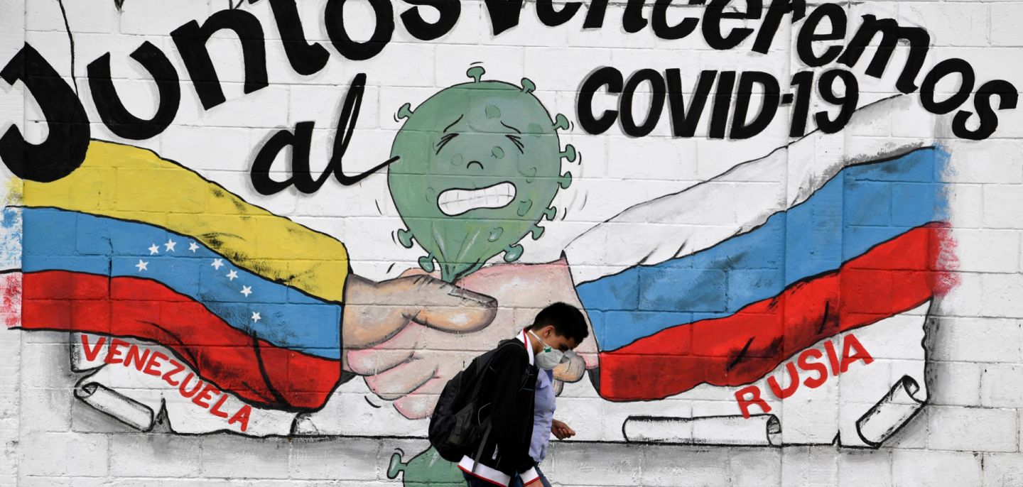 People walk past a mural of the Venezuelan and Russian flags that reads 