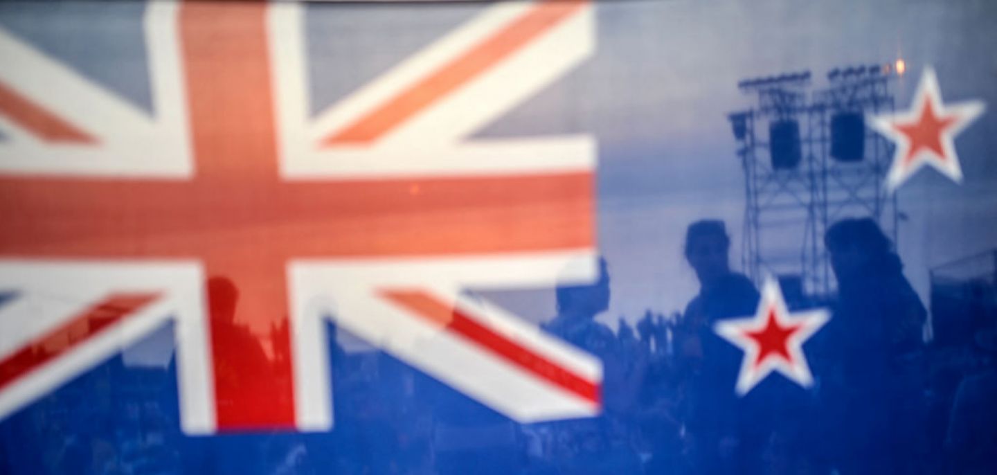 People are seen behind a New Zealand flag during a ceremony celebrating the anniversary of Anzac Day. 