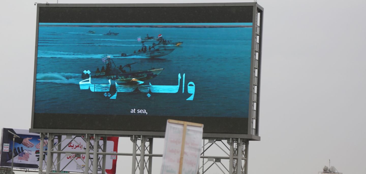 People in Sanaa, Yemen, stand under a large screen broadcasting Houthi-run coastguard forces patrolling in the Red Sea on March 13, 2026.