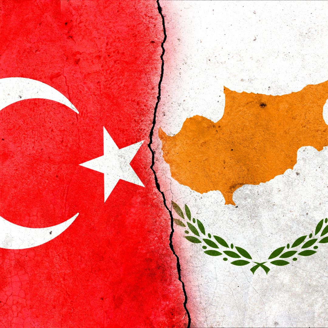The flags of the Turkish Republic of Northern Cyprus (L) and the Republic of Cyprus (R) are divided by a crack.