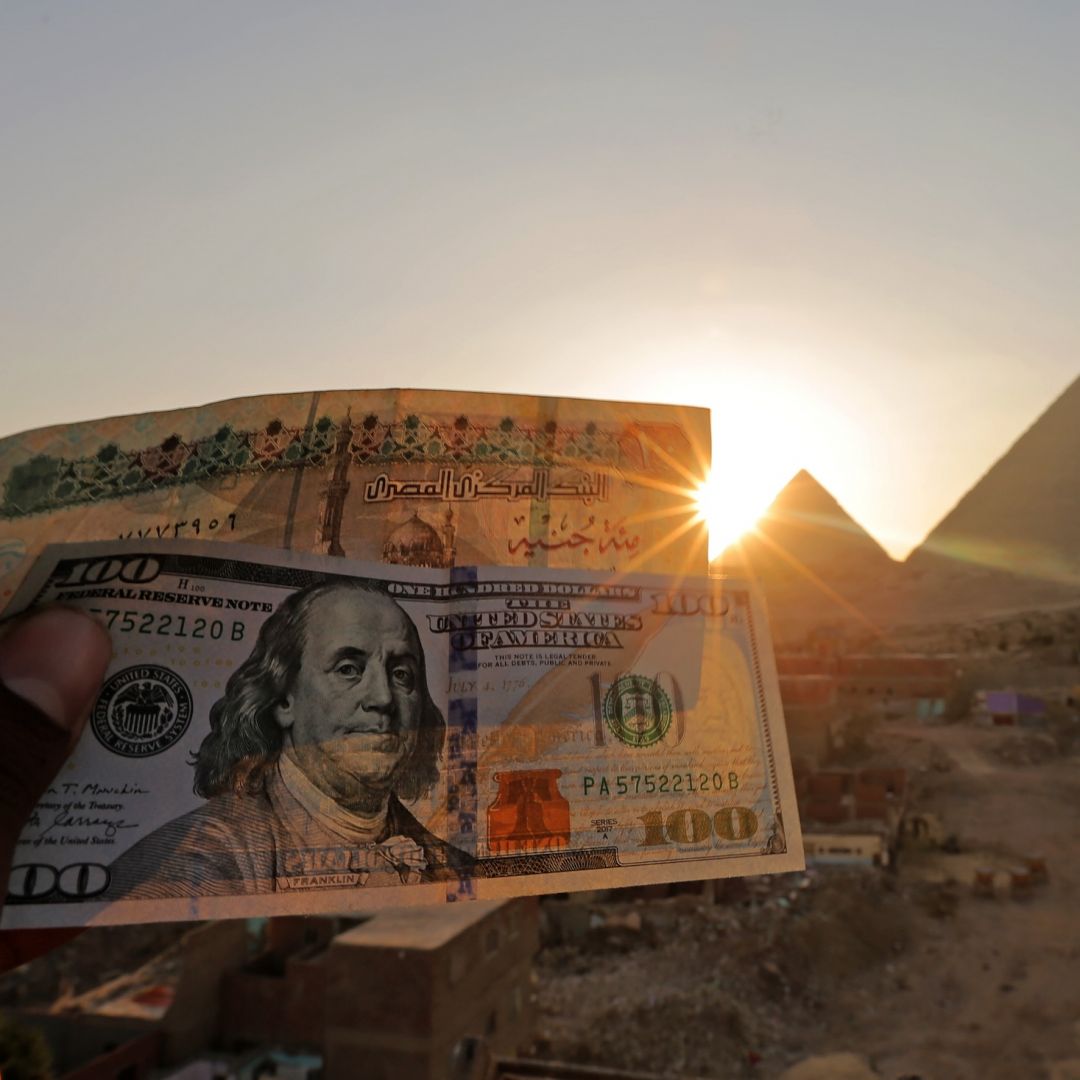 A 100-pound Egyptian banknote is held next to a $100 U.S. banknote near the Great Pyramids at Giza on Jan. 17, 2023.