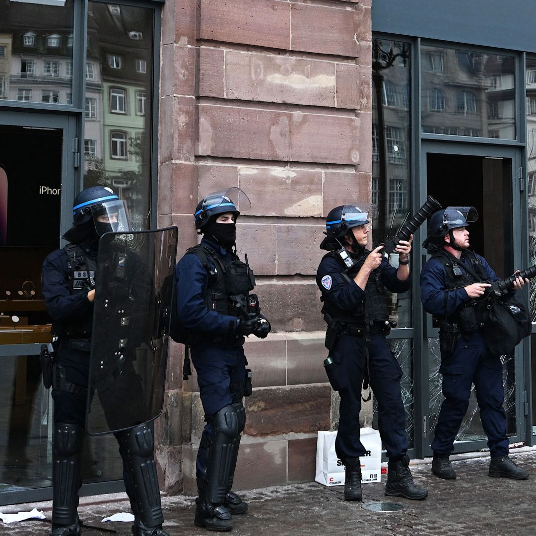 French police officers in riot gear stand guard and hold tear gas canister launchers next to the facade of a damaged Apple Store in Strasbourg, eastern France, on June 30, 2023.