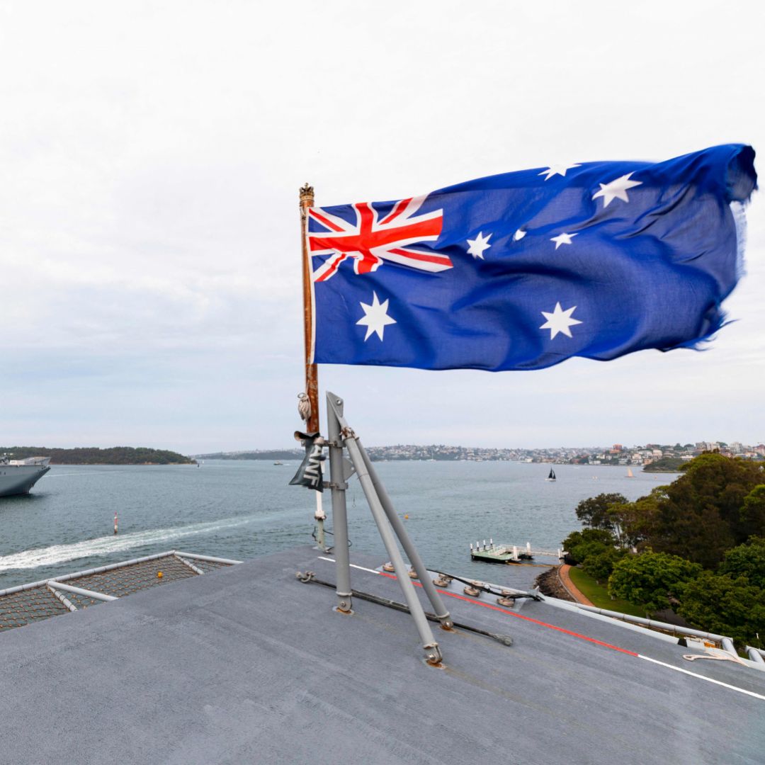 An Australian flag waves as a warship transits a waterway in the background in a photo taken on Jan. 18, 2020. 