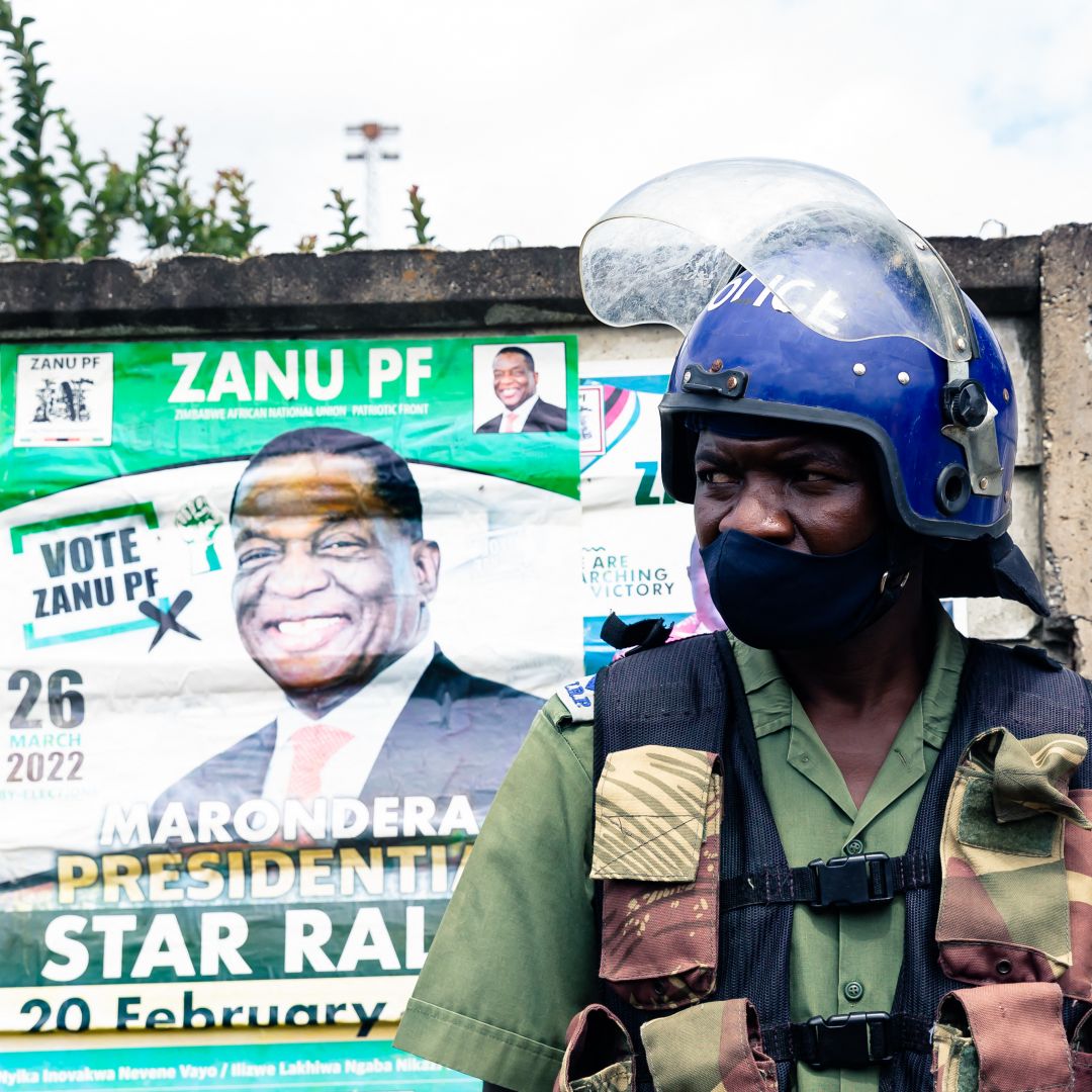 A police officer stands in front of an election poster for Zimbabwean President Emmerson Mnangagwa as he patrols outside a stadium where opposition leader Nelson Chamisa was holding a campaign rally in Marondera, Zimbabwe, on March 12, 2022. 