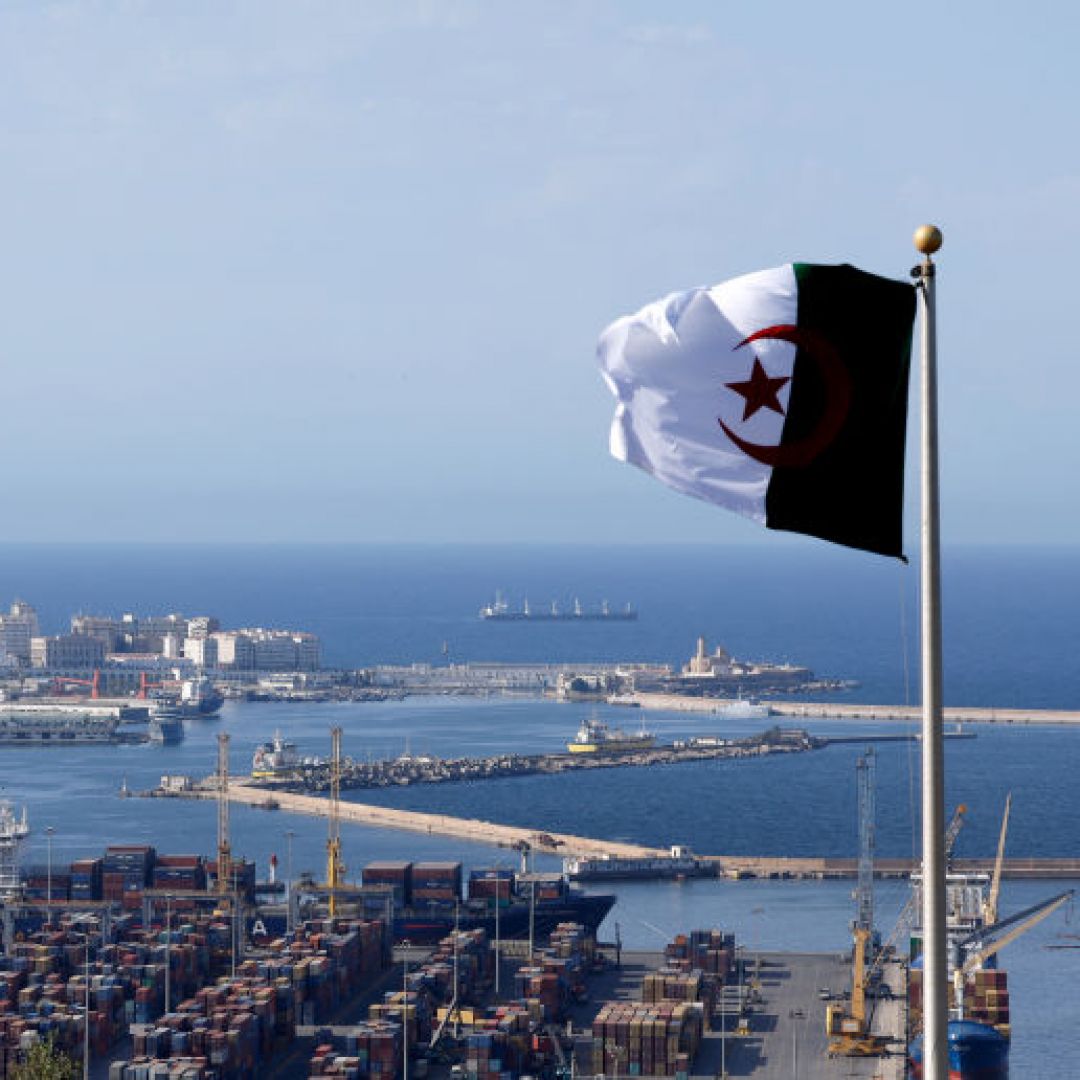 The national flag of Algeria flies near the Bay of Algiers against the backdrop of the old town known as the Casbah and cargo containers in Algiers, Algeria, on Aug. 25, 2022.