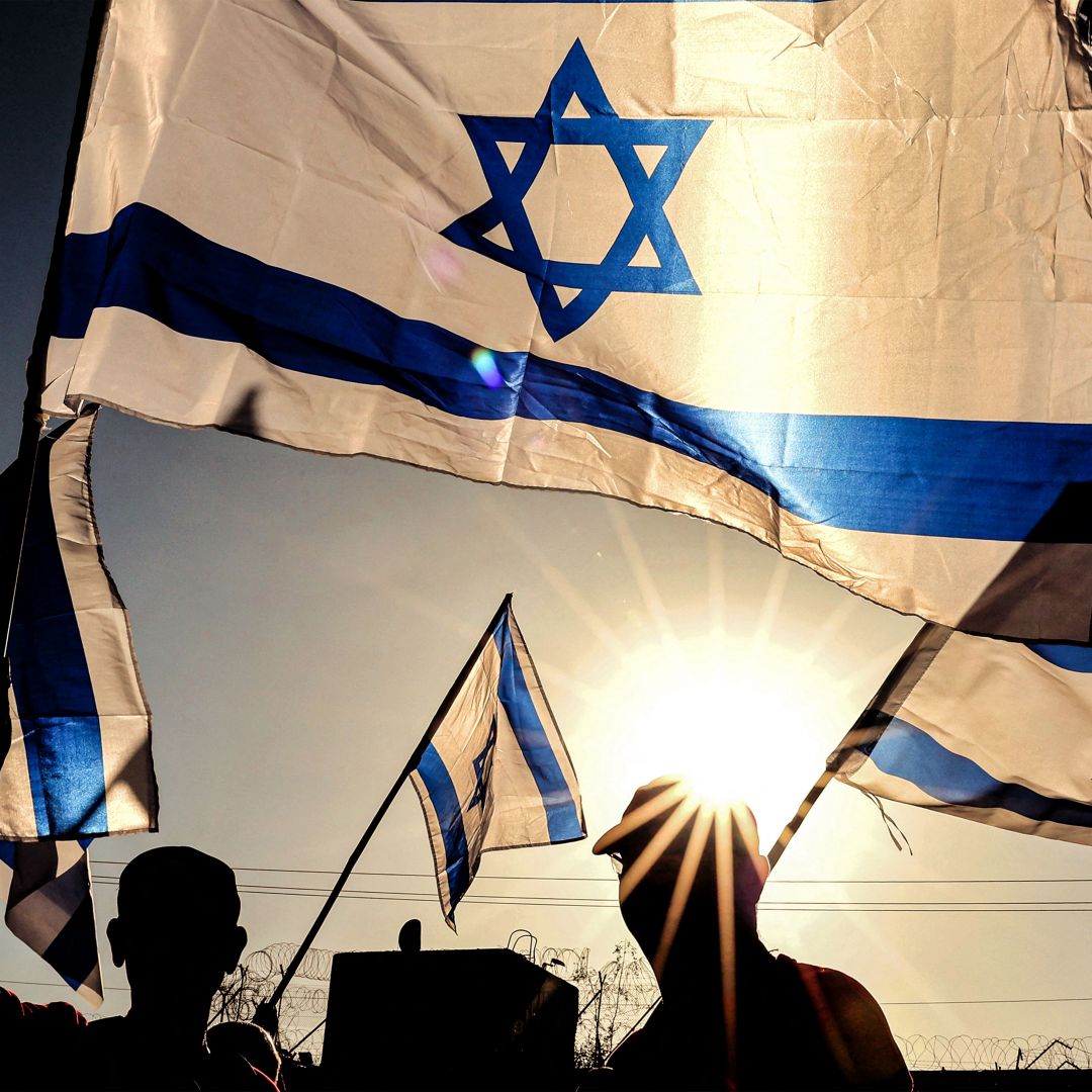 Israeli military veterans wave national flags during a rally against the government's judicial reform bill along a highway near Netanya on March 28, 2023.