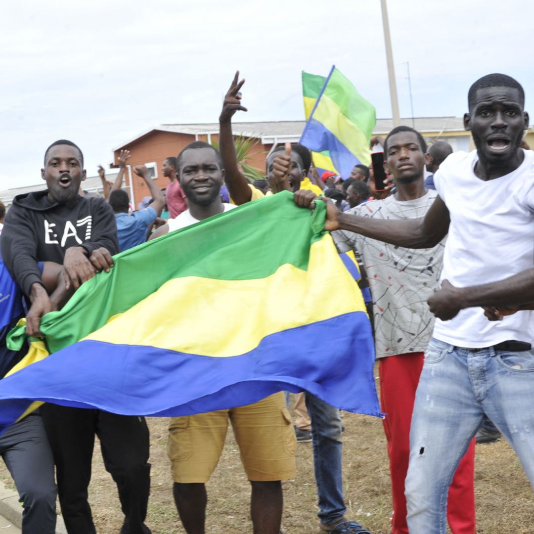 People hold up Gabon's national flag in the country's capital of Libreville on Aug. 30, 2023, as they celebrate after a group of military officers announced they were ''putting an end to the current regime'' and scrapping official election results that had handed another term to President Ali Bongo Ondimba. 