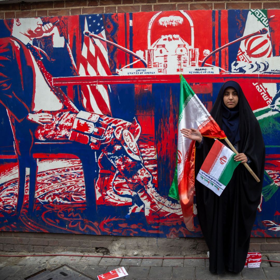 A woman holding an Iranian flag poses in front of an anti-U.S. mural on a wall of the former U.S. embassy in Tehran, Iran, on Nov. 4, 2023. 