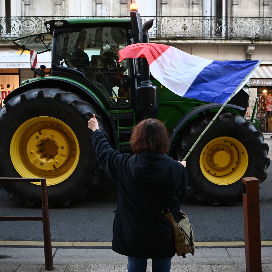 A woman waves a French flag in support of protesting farmers as a tractor drives by in Agen, southwerstern France, on Jan. 25, 2024.