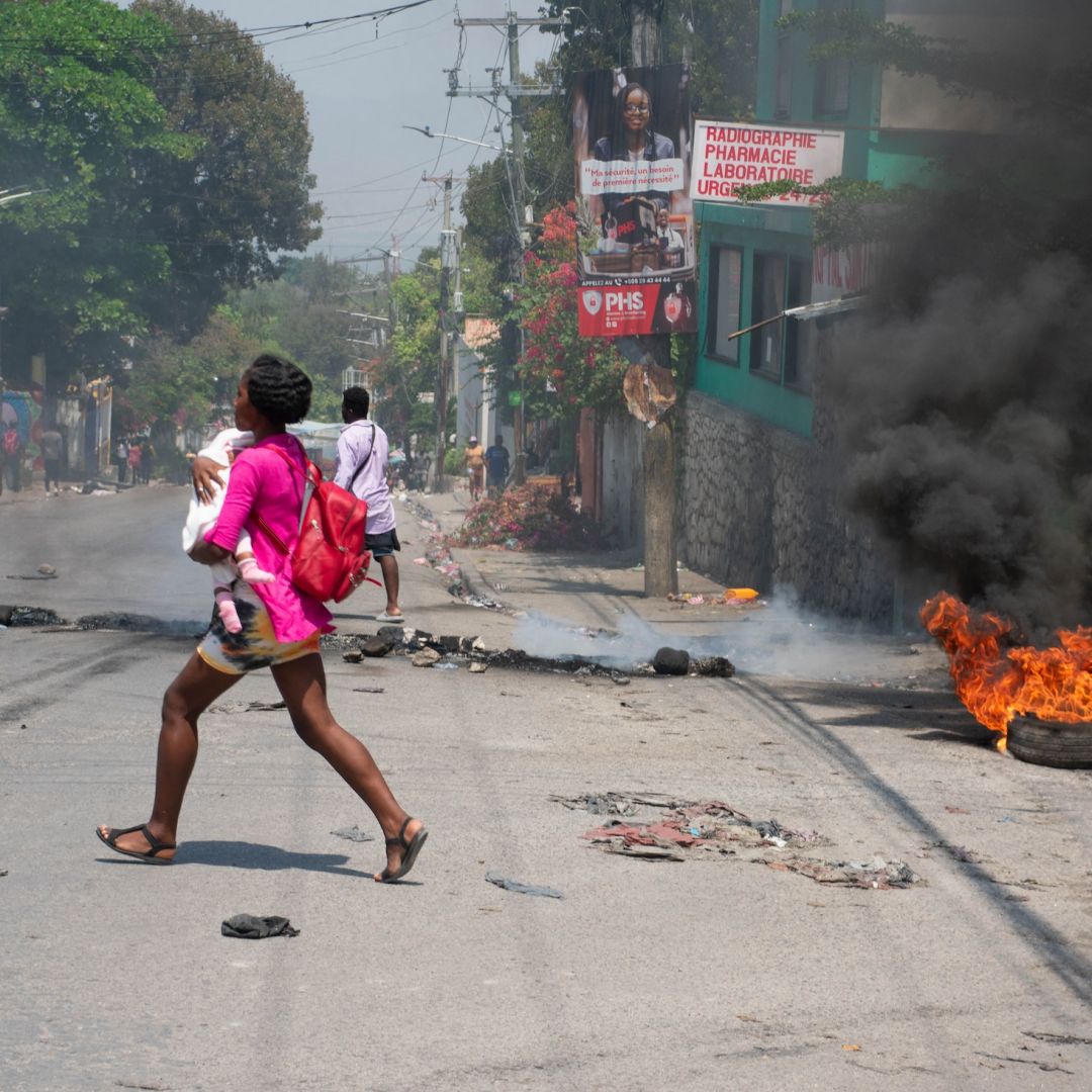 A woman carrying a child runs from an area in Port-au-Prince, Haiti, after hearing gunshots on March 20, 2024.