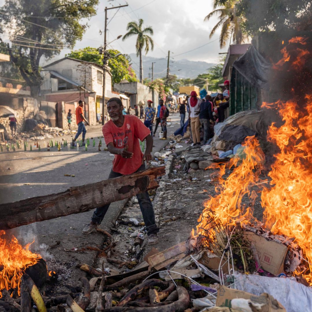 A man adds wood to a fire burning in the streets of Port-au-Prince, Haiti, on Oct. 3 amid protests demanding the resignation of Haitian Prime Minister Ariel Henry. 