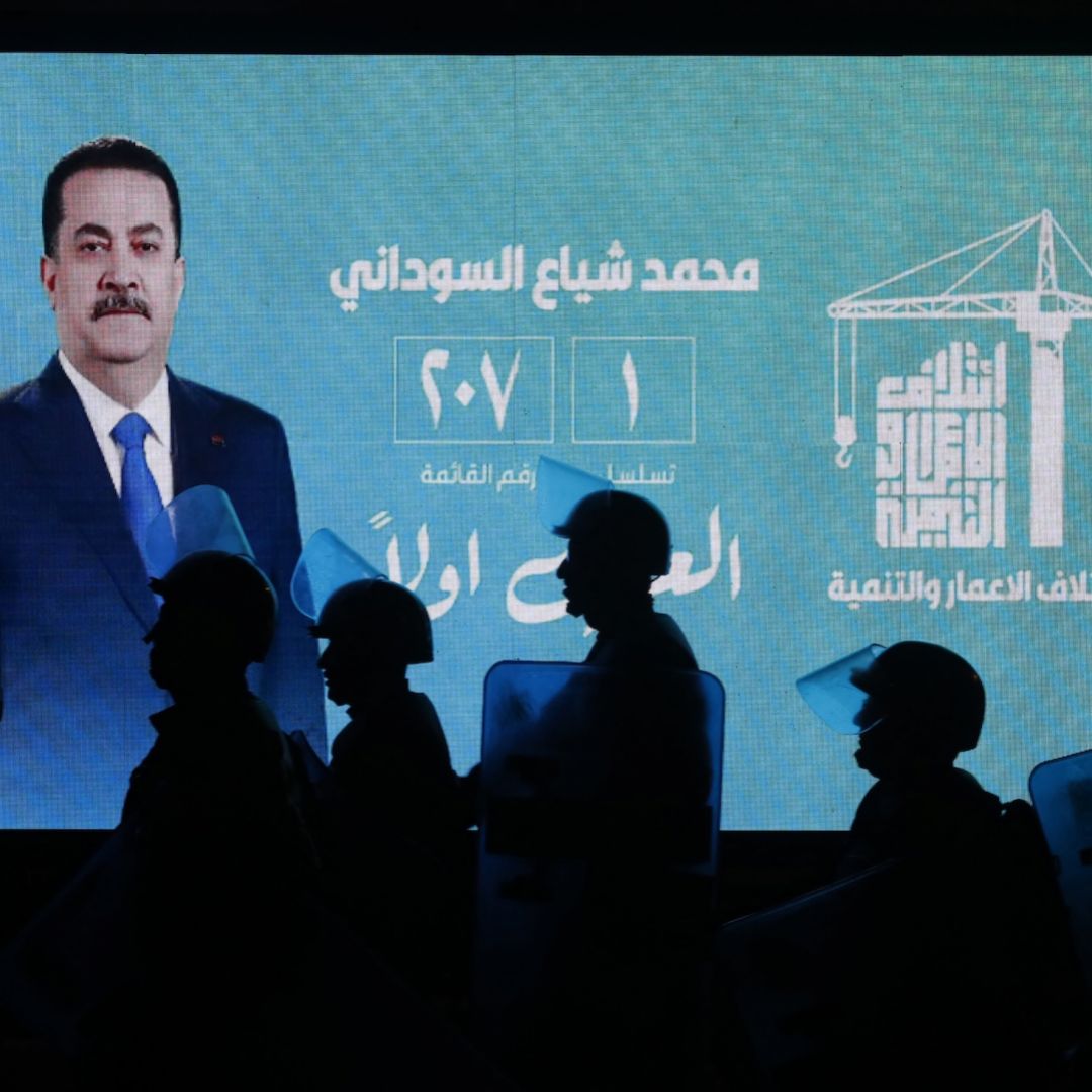 Iraqi riot police walk past a screen displaying a portrait of incumbent Iraqi Prime Minister Mohammed Shia al-Sudani during celebrations by his supporters following the announcement of preliminary election results in Baghdad on Nov. 12, 2025. Iraqi riot police walk past a screen displaying a portrait of incumbent Iraqi Prime Minister Mohammed Shia al-Sudani during celebrations by his supporters following the announcement of preliminary election results in Baghdad on Nov. 12, 2025.