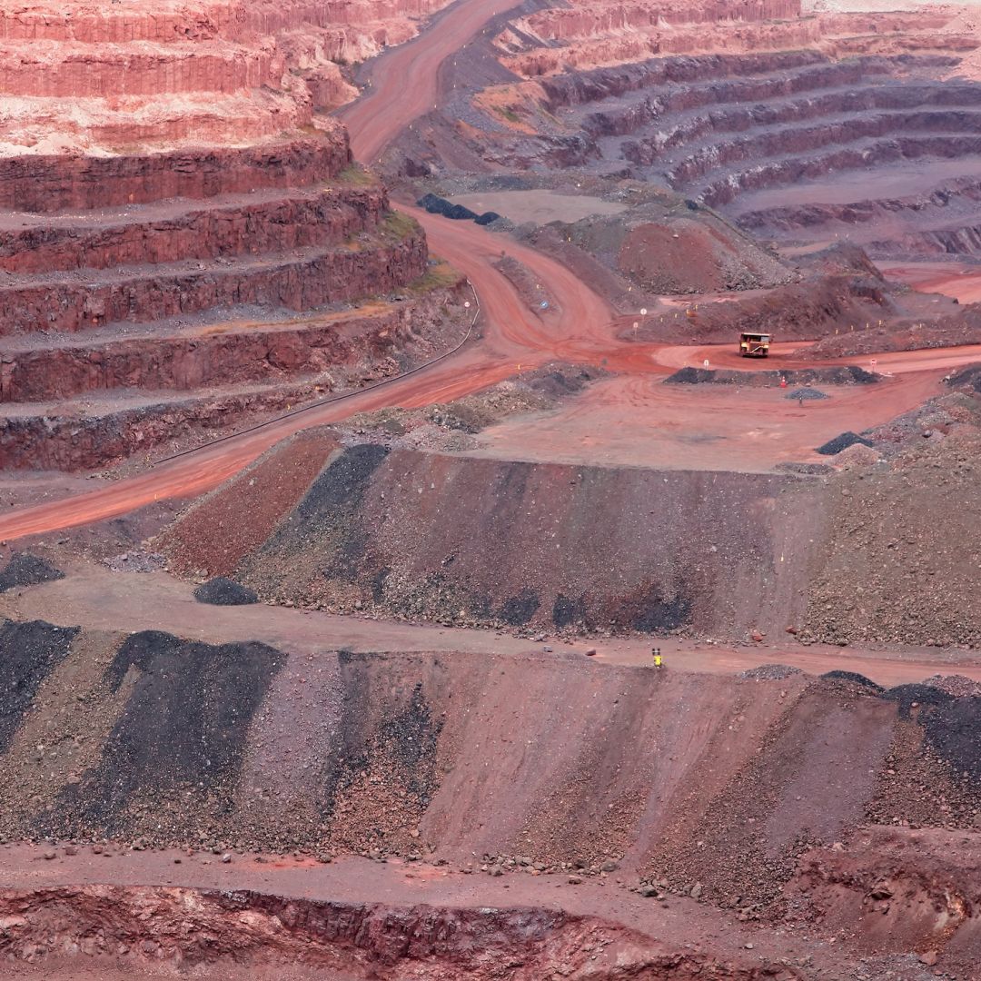 A stock photo shows a large, open-pit iron ore mine with various layers of soil.