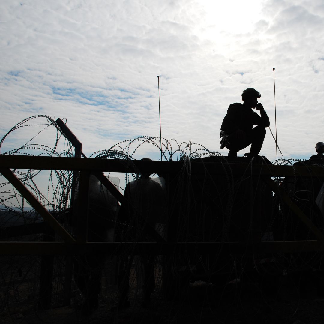 Israeli soldiers guard a barrier, silhouetted against afternoon sun.