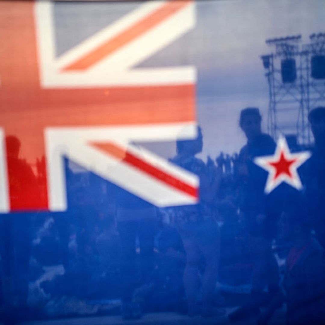 People are seen behind a New Zealand flag during a ceremony celebrating the anniversary of Anzac Day. People are seen behind a New Zealand flag during a ceremony celebrating the anniversary of Anzac Day.