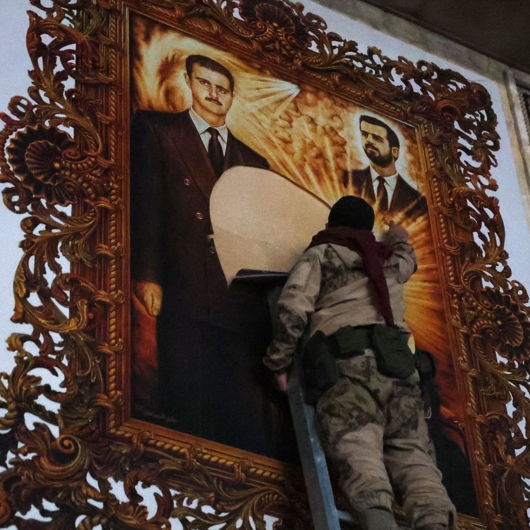 An anti-regime fighter tears off a poster depicting Syrian President Bashar al Assad (left) and his brother Maher at the airport in the northern Syrian city of Aleppo on Dec. 2, 2024. 