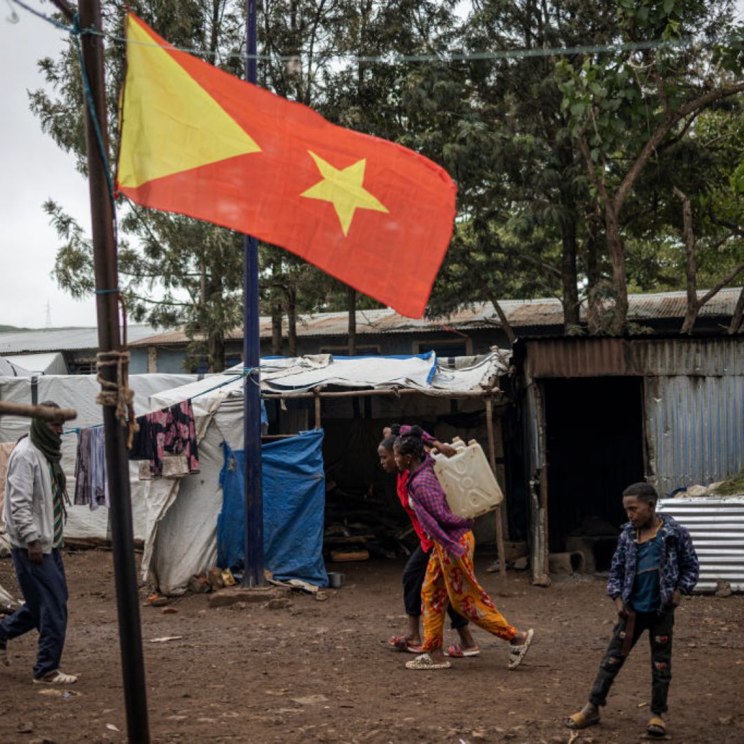 Internally displaced people walk past the Tigrayan flag at the Tsehaye camp in Ethiopia's Shire, Tigray region, on July 16, 2024. 