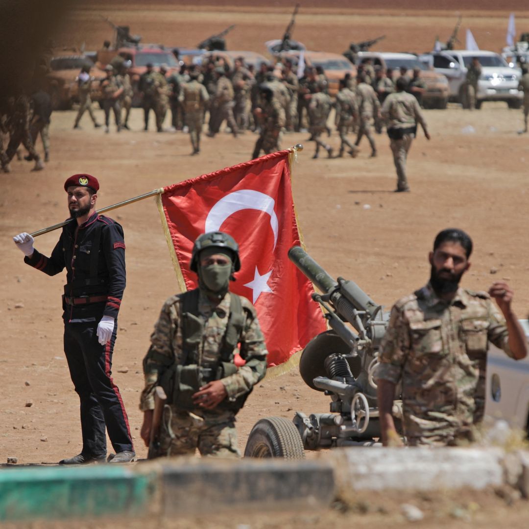 A man carries a Turkish national flag as Turkey-backed Syrian fighters gather along the frontlines opposite Kurdish forces near the town of Dadat in Syria's northern Aleppo province, on July 5, 2022. 